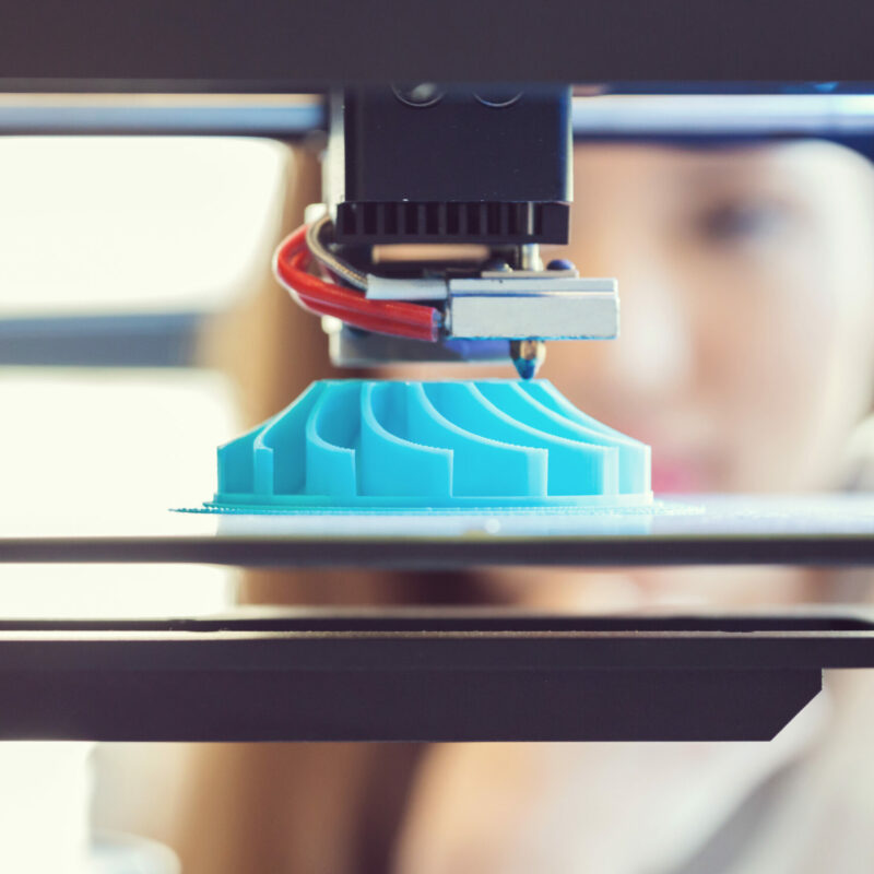 Young woman watching 3D printout. Focus on blue printout.